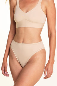 Against a white studio backdrop, Meagan wears the Bliss French Cut underwear in Beige with the Bliss bra in Beige, showing the high-cut leg openings and smooth fabric in a close-up angled pose.