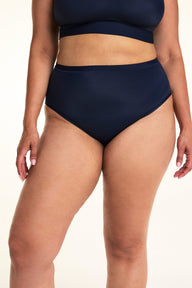 On a light studio backdrop, Jennifer wears the Bliss Highwaist in Navy. The close-up front view highlights the high-rise waistband, smooth fabric, and full-coverage silhouette.