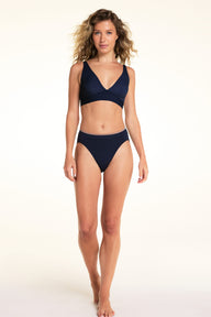 On a light studio backdrop, Alexis wears the Bliss Plunge Adjustable Bralette in Navy with matching underwear. Standing facing forward, she shows the plunge neckline, adjustable fit, and wide underband.