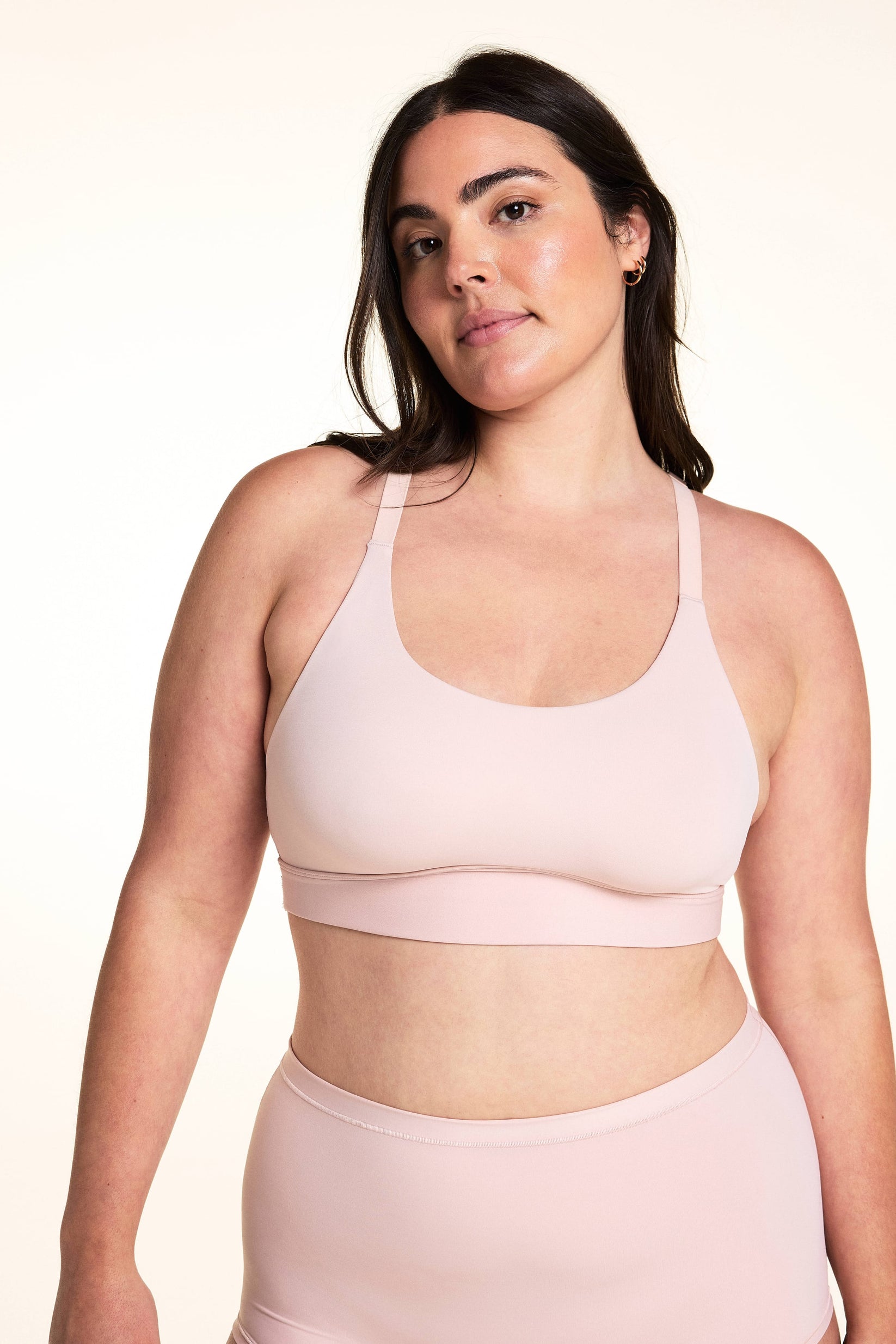 On a light studio backdrop, Alessandra wears the Bliss Racerback Bralette in Ember Rose with matching high-rise bottoms. The front view highlights the scoop neckline, smooth fabric, adjustable straps, and wide comfort band. sizing: Alessandra wears size Large