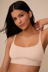 On a neutral beige backdrop, a close-up of Marcela wearing the Bliss Scoop Adjustable Bralette in Beige highlights the scoop neckline, adjustable straps, and soft, smooth fabric.