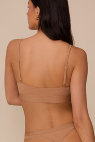 On a neutral beige backdrop, a back view of Marcela wearing the Bliss Scoop Adjustable Bralette in Tan highlights the adjustable straps, wide underband, and smooth back construction.