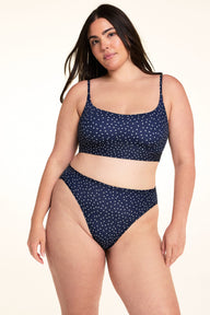 On a light studio backdrop, Alessandra wears the Bliss Scoop Bralette in Navy Dot with matching Navy Dot underwear. The full-body image showcases the scoop neckline, adjustable straps, and allover white dot print.