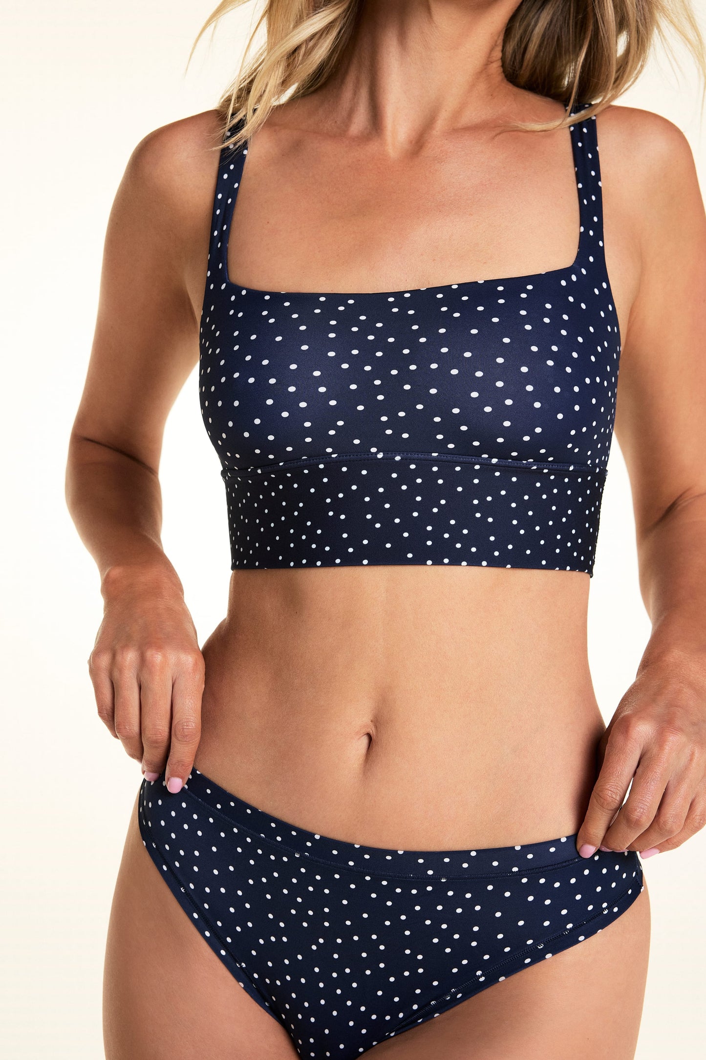 On a light studio backdrop, Meagan wears the Bliss Square Neck Bralette in Navy Dot with matching Navy Dot underwear. The close-up image highlights the square neckline, wide underband, and allover white dot print.