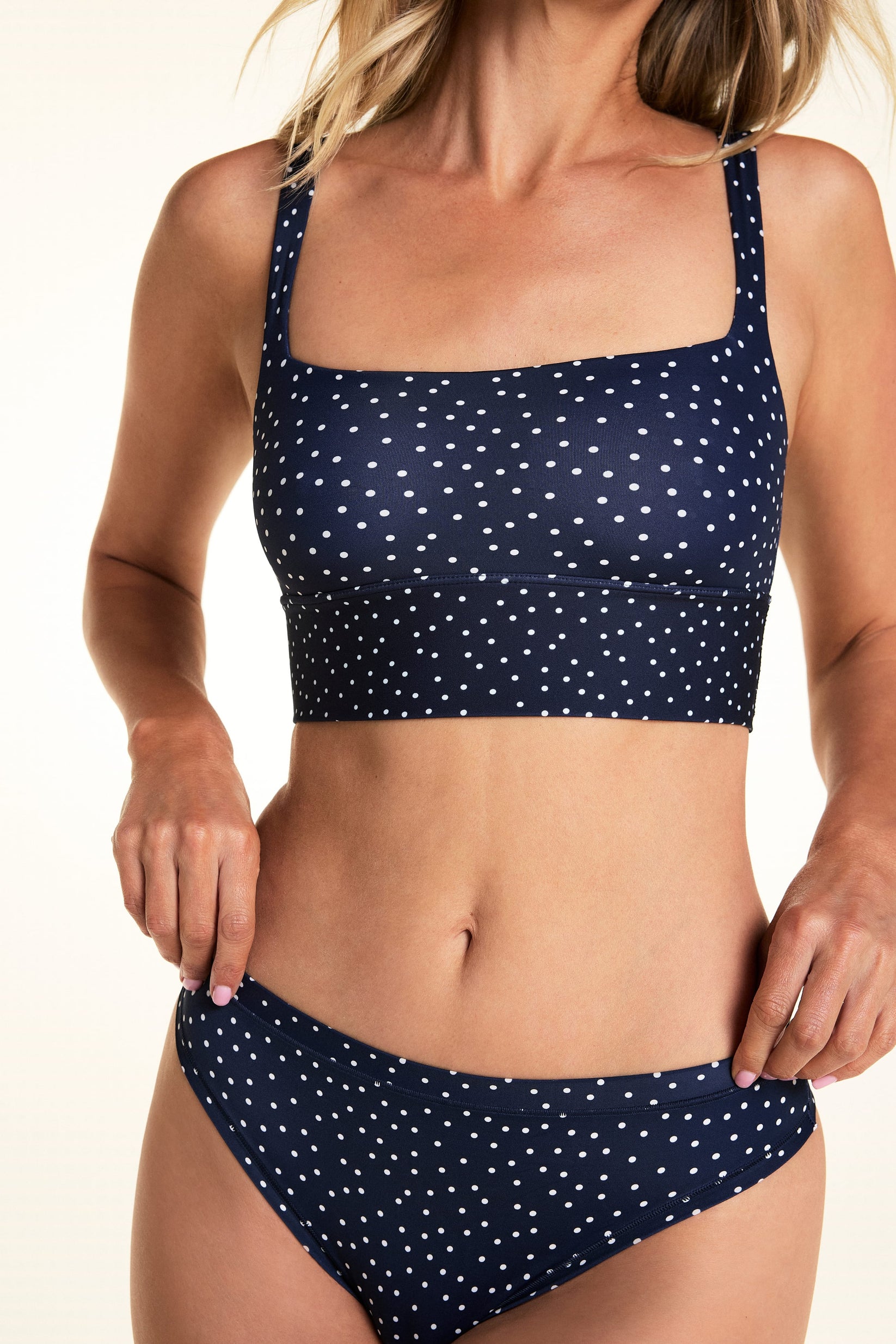 On a light studio backdrop, Meagan wears the Bliss Square Neck Bralette in Navy Dot with matching Navy Dot underwear. The close-up image highlights the square neckline, wide underband, and allover white dot print.