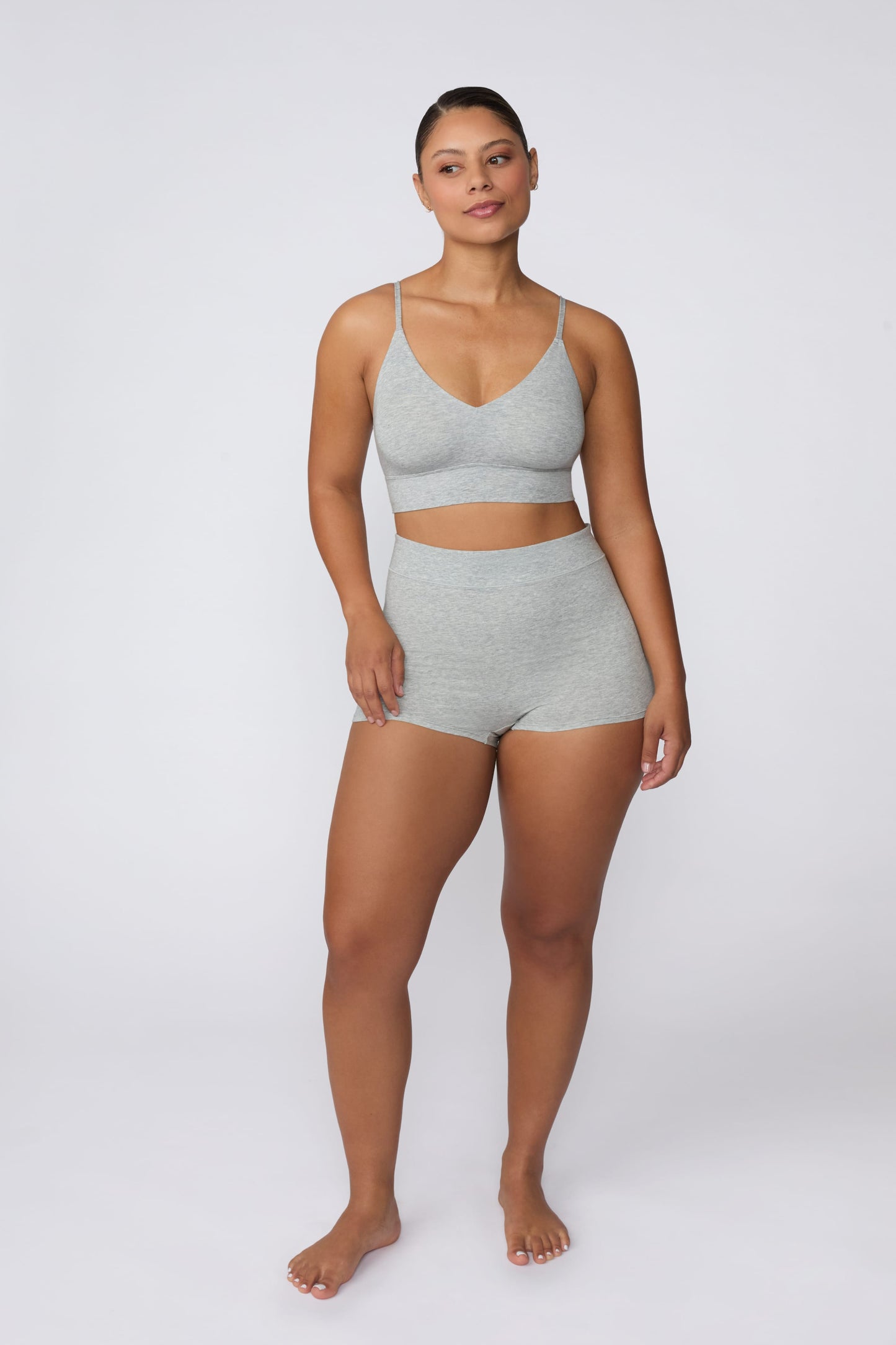 On a light gray studio backdrop, India wears the Cloud Cotton Boyshort in Heather Grey. The full-body front view highlights the high-rise waistband, soft cotton fabric, and longer leg coverage.