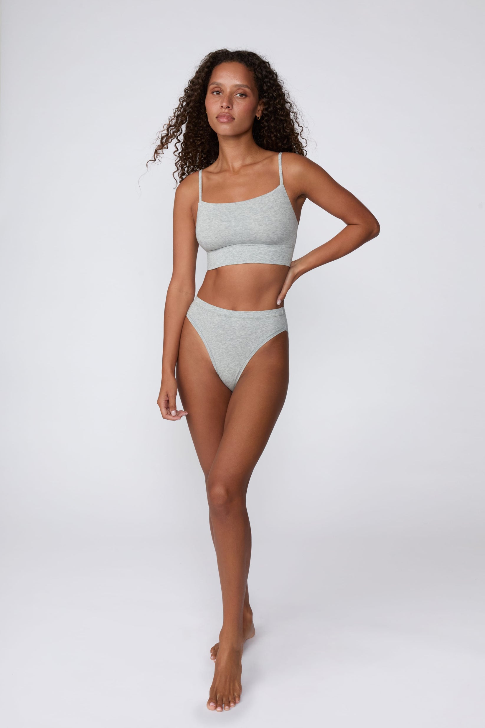 On a light gray studio backdrop, Courtney wears the Cloud Cotton French Cut Brief in Heather Grey with the matching Cloud Cotton Thin Strap Bralette. The full-body view highlights the French-cut silhouette, mid-rise fit, and soft cotton fabric.