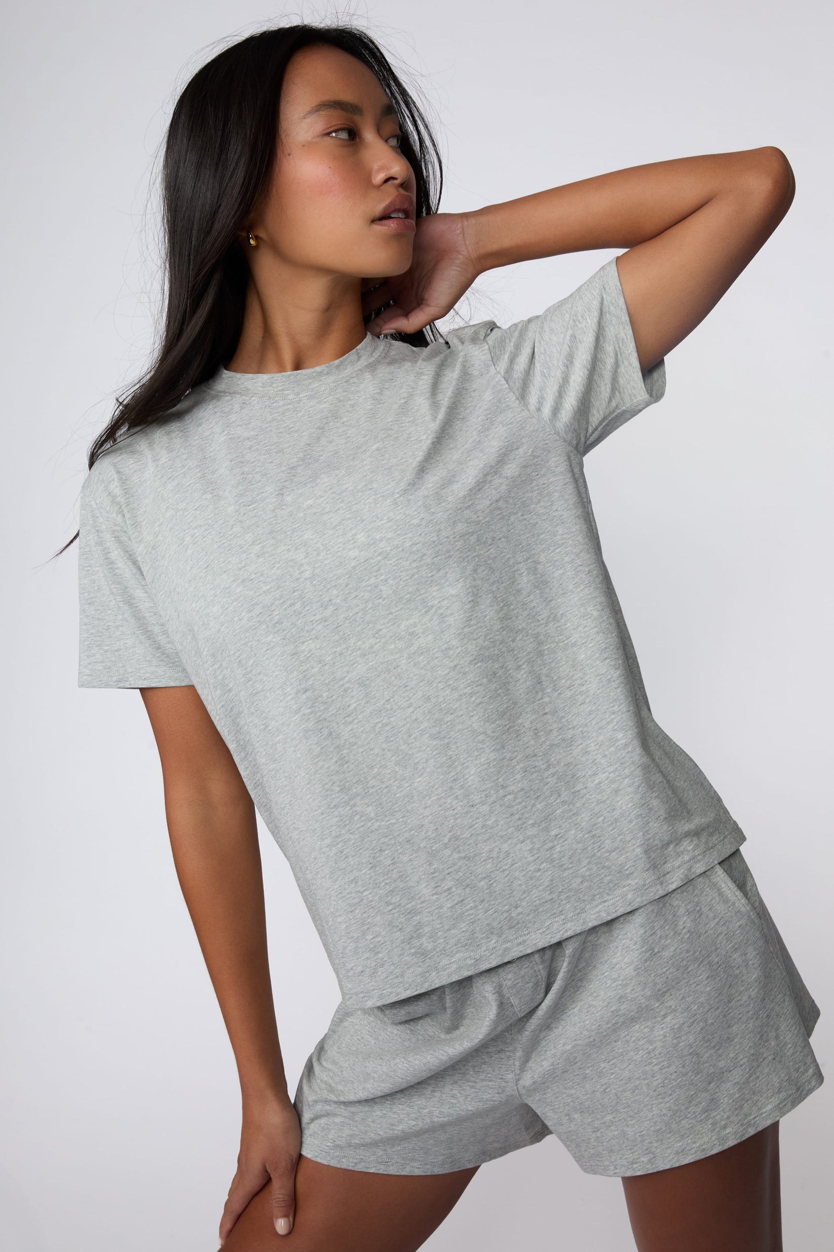 On a light gray studio backdrop, Amber wears the Cloud Cotton Pajama Shirt in Heather Grey with matching pajama shorts. The close-up view highlights the crew neckline, short sleeves, and soft cotton fabric.