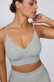 On a light gray studio backdrop, India wears the Cloud Cotton Triangle Bralette in Heather Grey with matching high-rise shorts. The full-body view highlights the soft cotton fabric, deep V-neckline, and wide underband.