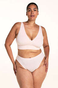 On a light studio backdrop, Jennifer wears the Cloud Cotton Plunge Bralette in Dogwood with matching Dogwood underwear. The image highlights the deep V-neck, smooth fabric, and wide comfort band.  sizing: Jennifer wears size XL