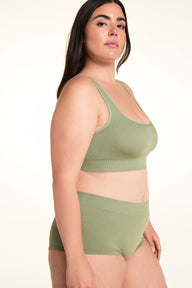On a white studio backdrop, Alessandra wears the Lounge Rib Scoop Bralette in Dill with the matching Lounge Rib Sleepshort in a side profile, highlighting the scoop neckline, wide straps, ribbed fabric, and supportive underband.