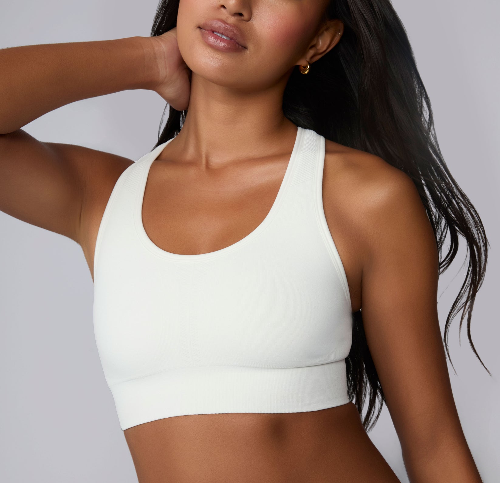 On a neutral studio backdrop, Amber is shown in a close-up front view wearing the Seamless Racerback Sports Bra in White. The smooth scoop neckline, wireless support, and wide underband are visible as she rests one hand at her neck.