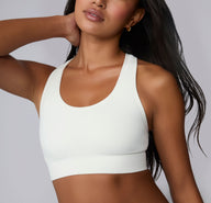 On a neutral studio backdrop, Amber is shown in a close-up front view wearing the Seamless Racerback Sports Bra in White. The smooth scoop neckline, wireless support, and wide underband are visible as she rests one hand at her neck.