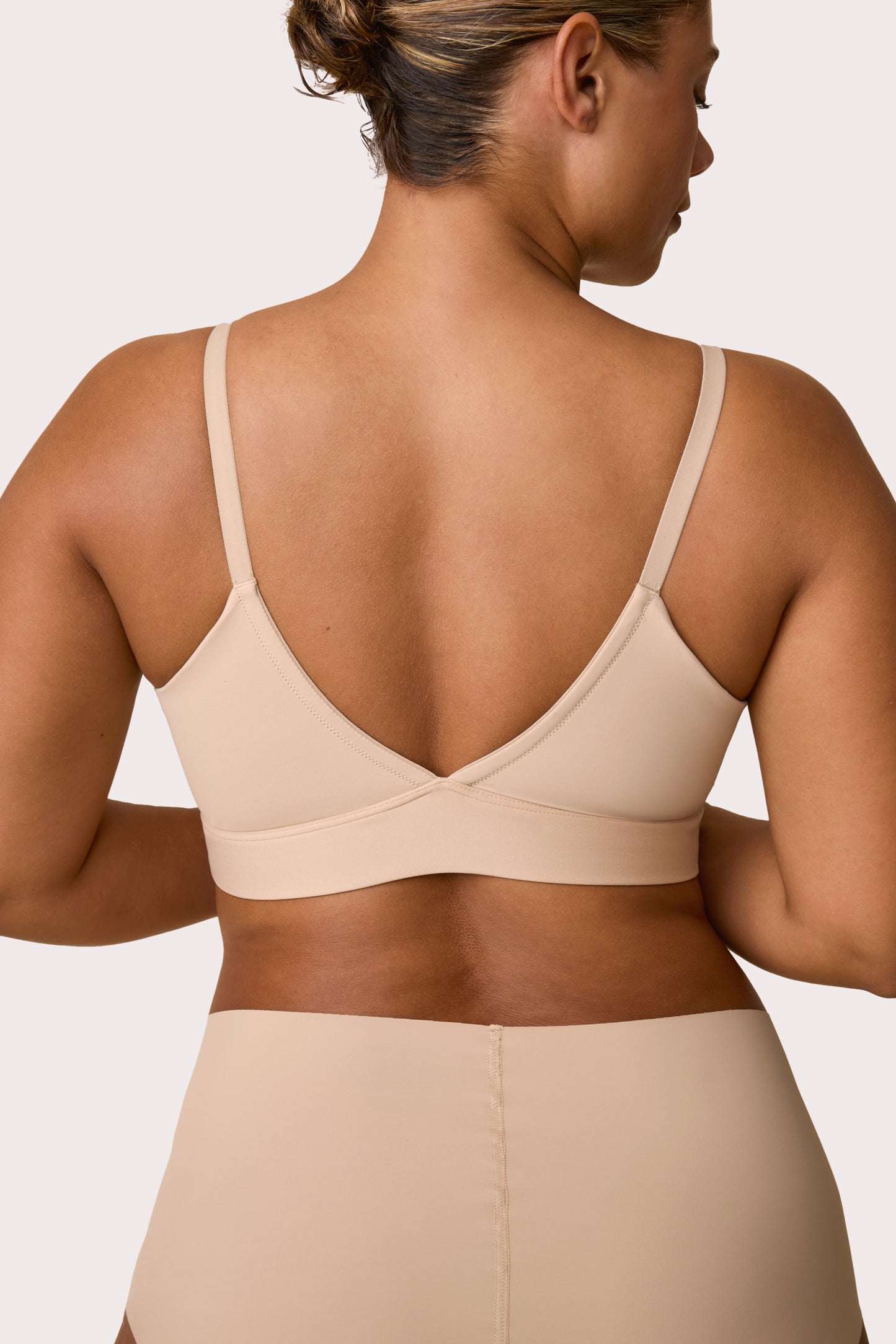 From the back on a white studio backdrop, India wears the Bliss Triangle Bralette in Beige with the matching brief, showing the low-back V shape, adjustable straps, and smooth microfiber band. sizing: India wears size Large