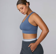 On a light gray studio backdrop, India wears the Seamless Racerback Sports Bra in Evernight, shown in side profile to highlight the smooth scoop neckline, wide underband, and racerback silhouette. The soft, supportive fabric sits comfortably against the body for low-impact movement and everyday wear. sizing:India wears size Large