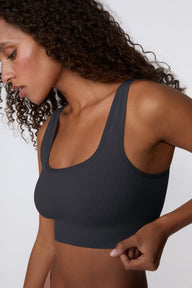 On a light gray studio backdrop, Courtney wears the Ribbed Seamless Scoop Bralette in Charcoal. A close-up side view highlights the scoop neckline, wide straps, ribbed texture, and supportive underband.