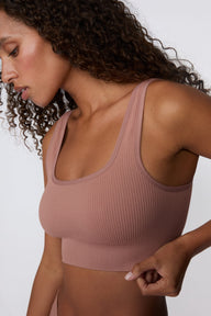 On a light gray studio backdrop, Courtney wears the Ribbed Seamless Scoop Bralette in Plum. A close-up side view highlights the scoop neckline, wide straps, ribbed texture, and supportive underband.