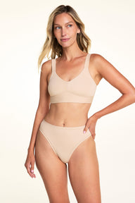 On a light neutral backdrop, Meagan wears the Bliss Smoothing Bralette in Beige with matching underwear. She stands facing forward, showing the V-neckline, wide straps, and smooth wireless design.