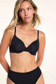 On a light studio backdrop, Meagan wears the Base Picot T-Shirt Bra in Black. The three-quarter front view highlights the smooth molded cups, picot trim along the neckline, and adjustable straps.