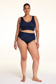 On a light studio backdrop, Jennifer wears the Bliss Bralette in Navy with matching underwear. Standing facing forward, she shows the V-neckline, wireless support, and smooth, comfortable fit.