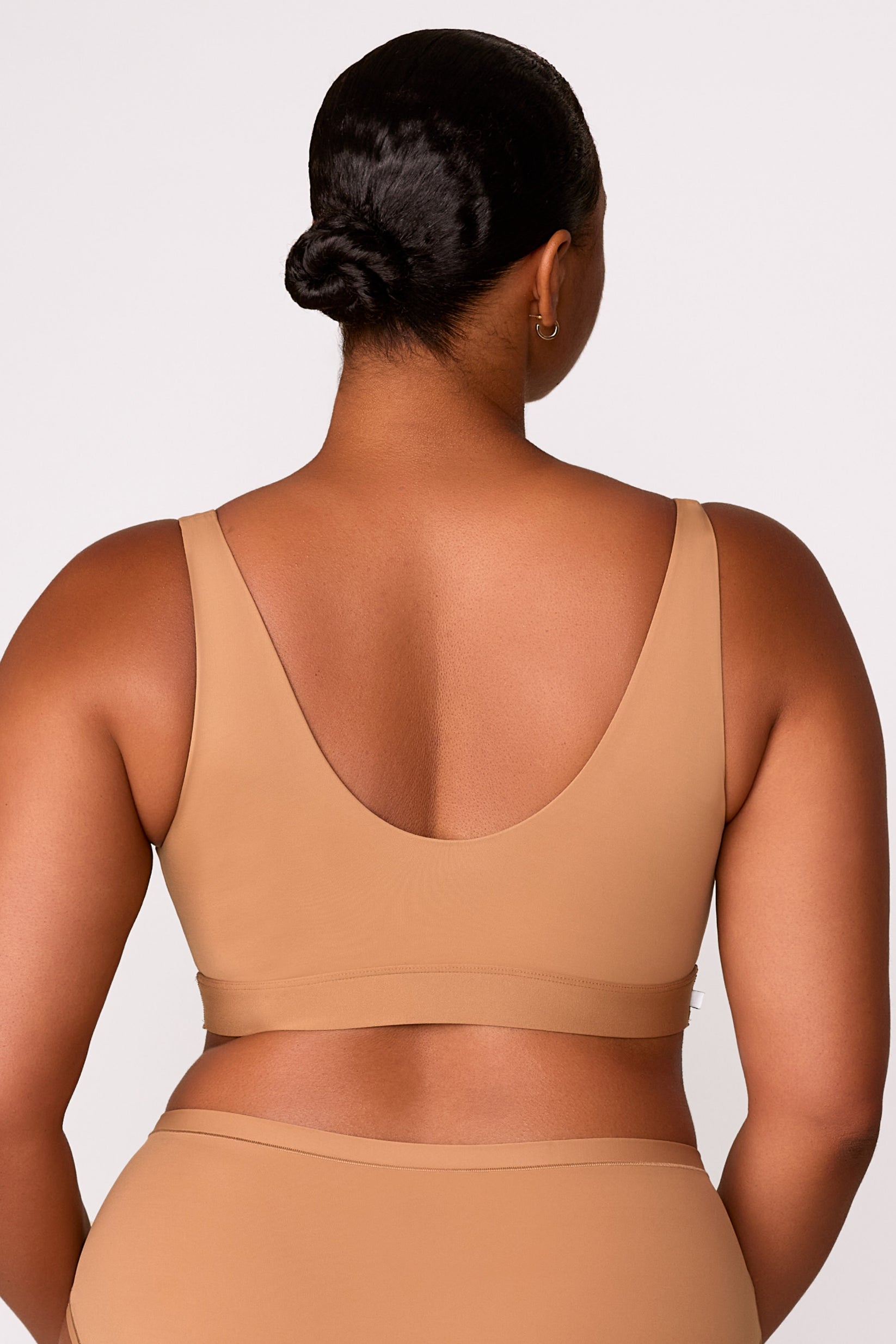 On a white studio backdrop, Zarria wears the Bliss Bralette in Tan, showing the wide straps, and smooth fabric from the back.