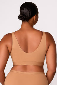 On a white studio backdrop, Zarria wears the Bliss Bralette in Tan, showing the wide straps, and smooth fabric from the back.