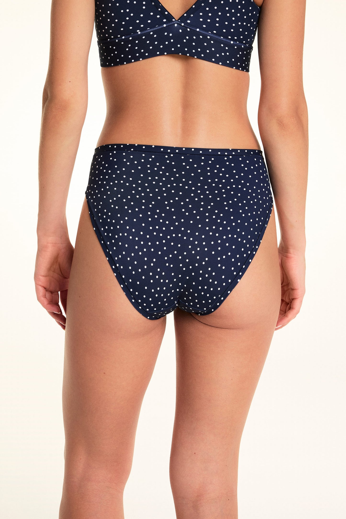 On a light studio backdrop, Alexis wears the Bliss French Cut in Navy Dot with a matching Navy Dot bralette. The back view highlights the full back coverage, smooth waistband, and allover white dot print.
