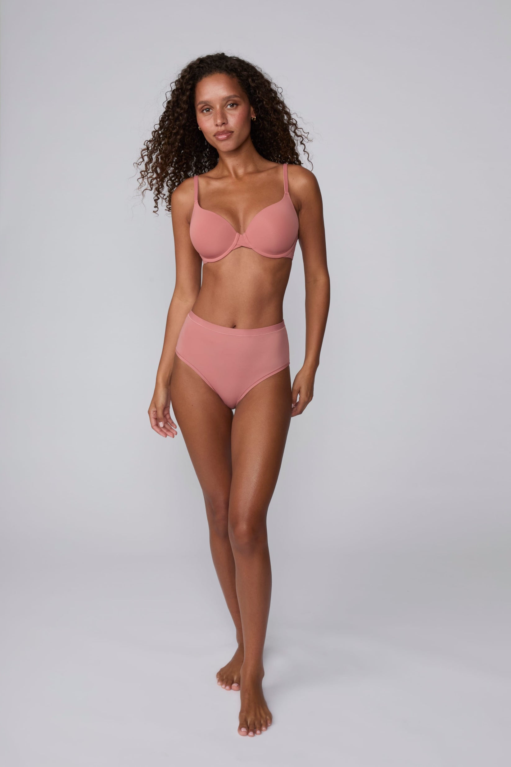 On a light gray studio backdrop, Courtney wears the Bliss Highwaist Brief in Cinnamon with a matching bra. A full-body front view highlights the smooth fabric, high-rise waistband, and full-coverage design.