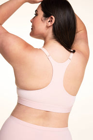 On a light studio backdrop, Alessandra wears the Bliss Racerback Bralette in Ember Rose, shown from the back to highlight the racerback design, adjustable straps, and smooth back band.