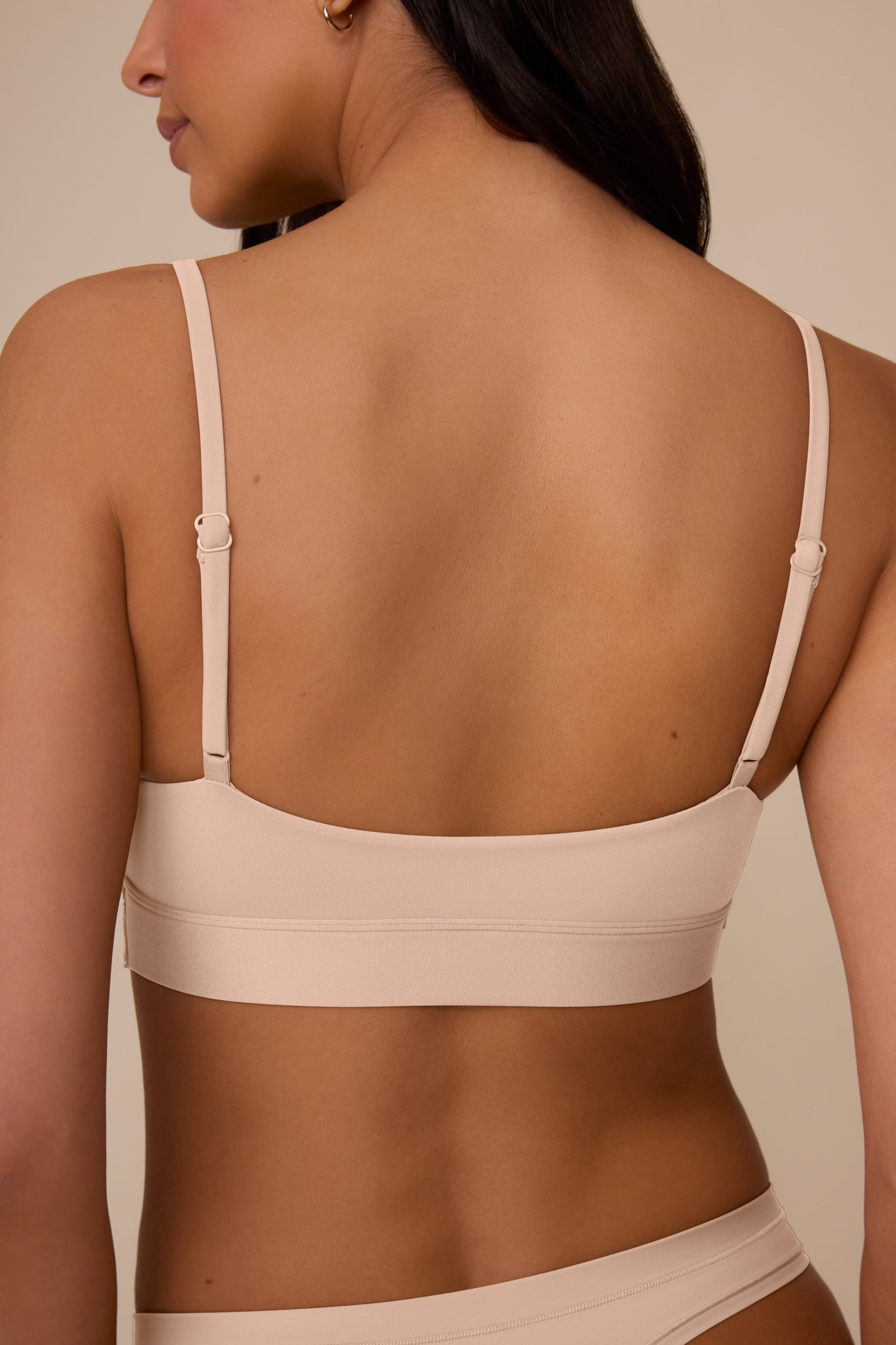 On a neutral beige backdrop, a back close-up of Marcela wearing the Bliss Scoop Adjustable Bralette in Beige showcases the adjustable straps, wide underband, and smooth back construction.