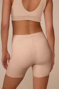 On a neutral studio backdrop, Marcela wears the Bliss Under Short in Beige with a matching beige bralette. The close-up back view highlights the smooth waistband, clean lines, and full coverage through the back and thighs.