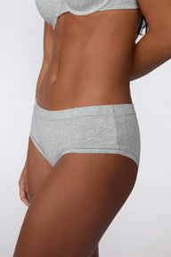 In a studio setting, Amber wears the Cloud Cotton Hiphugger in Heather Grey with the matching bra. The side view highlights the hiphugger silhouette, low-rise fit, and soft cotton fabric.