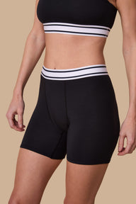 On a neutral studio backdrop, Gracie wears the Cloud Cotton Retro Boxer Brief in Black. The close-up front view highlights the full-coverage boxer brief silhouette, smooth cotton modal fabric, and retro-inspired logo waistband with contrasting stripes.