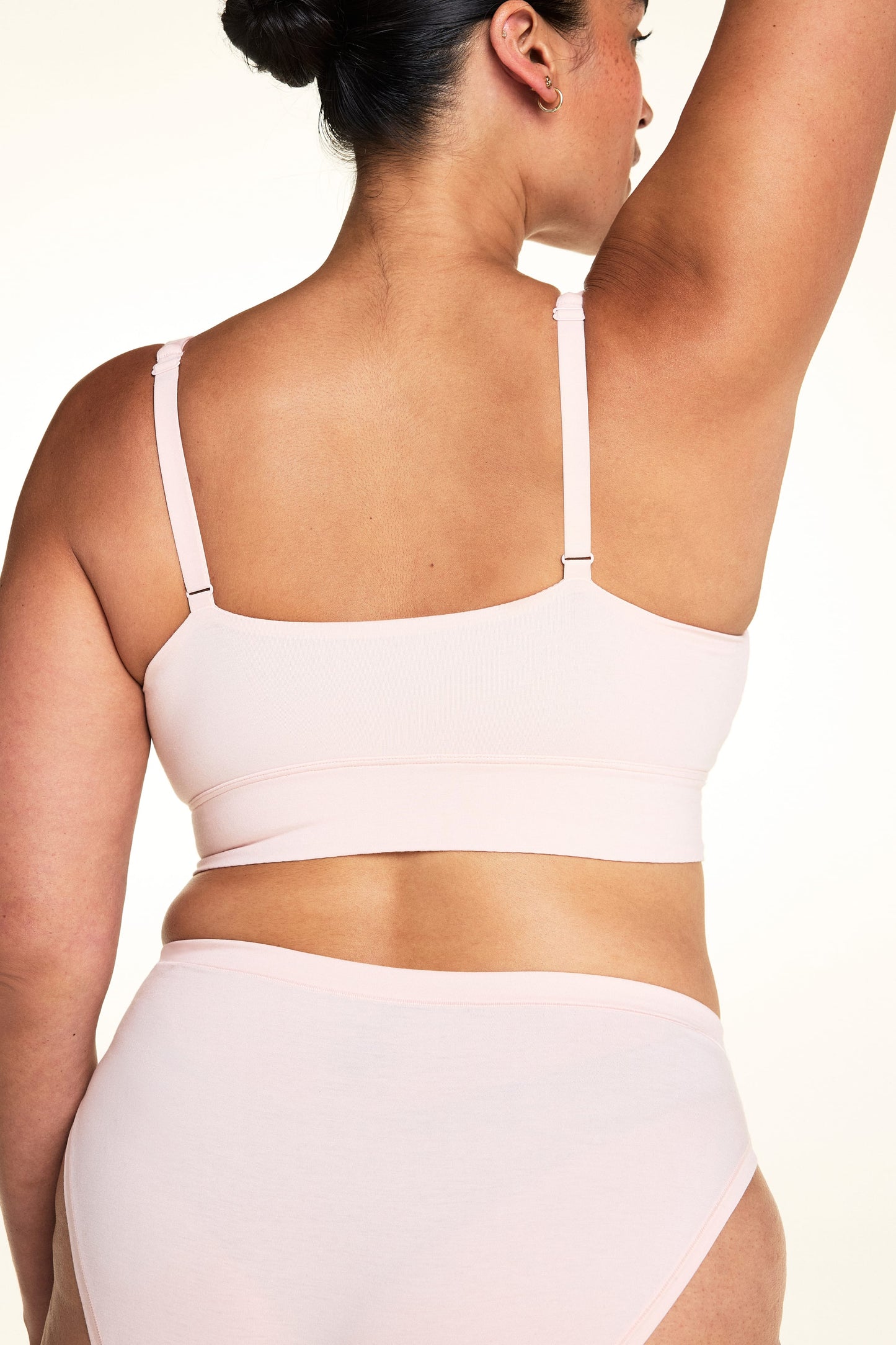 On a light studio backdrop, Jennifer wears the Cloud Cotton Plunge Bralette in Dogwood with matching Dogwood underwear. The back view highlights the adjustable straps, smooth fabric, and wide comfort band.