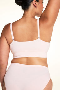 On a light studio backdrop, Jennifer wears the Cloud Cotton Plunge Bralette in Dogwood with matching Dogwood underwear. The back view highlights the adjustable straps, smooth fabric, and wide comfort band.