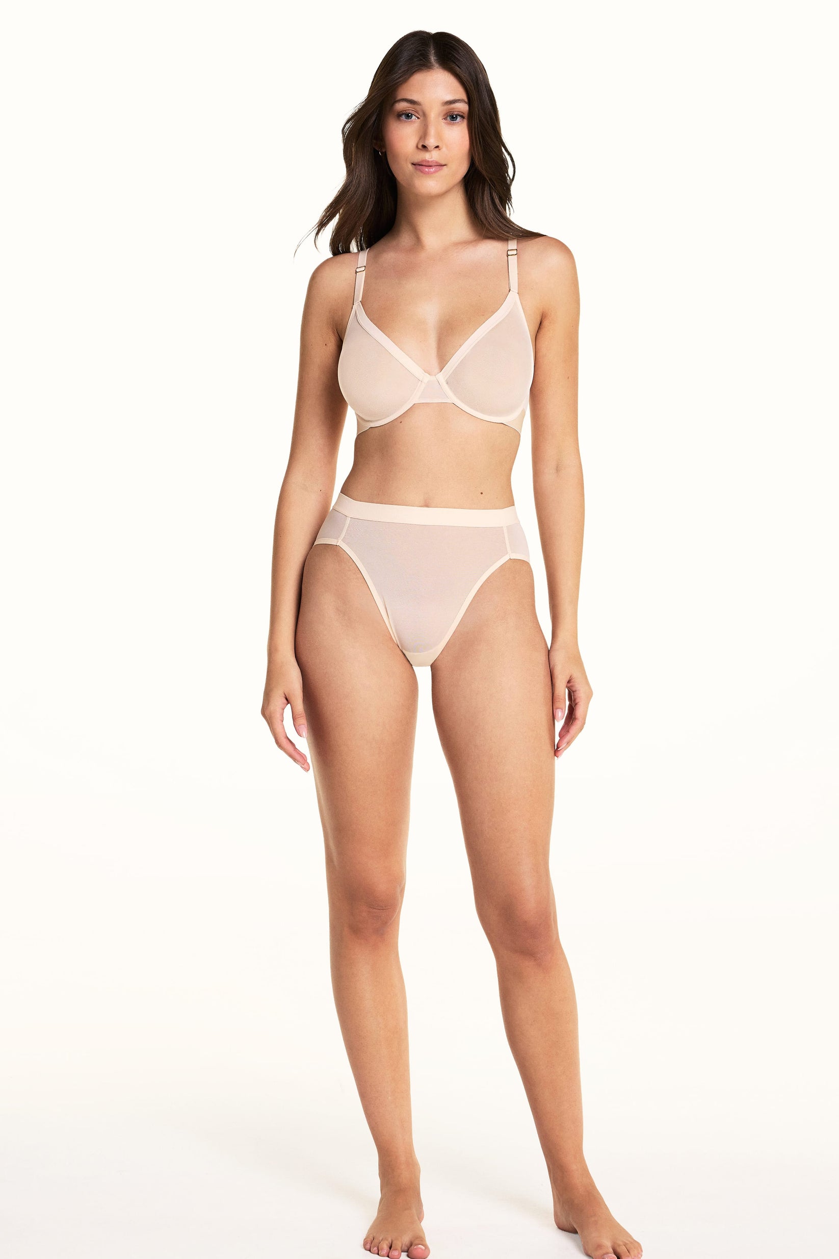 On a light studio backdrop, Laura wears the ComfortMesh™ Plunge Bra and ComfortMesh™ Highwaist Brief in Pearl. The full-body view highlights the sheer mesh fabric, plunging neckline, high-rise silhouette, and wide waistband.