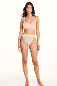 On a light studio backdrop, Laura wears the ComfortMesh™ Plunge Bra and ComfortMesh™ Highwaist Brief in Pearl. The full-body view highlights the sheer mesh fabric, plunging neckline, high-rise silhouette, and wide waistband.