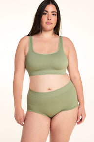 On a white studio backdrop, Alessandra wears the Lounge Rib Scoop Bralette in Dill with the matching Lounge Rib Sleepshort. The front view highlights the scoop neckline, wide straps, ribbed fabric, and supportive underband.