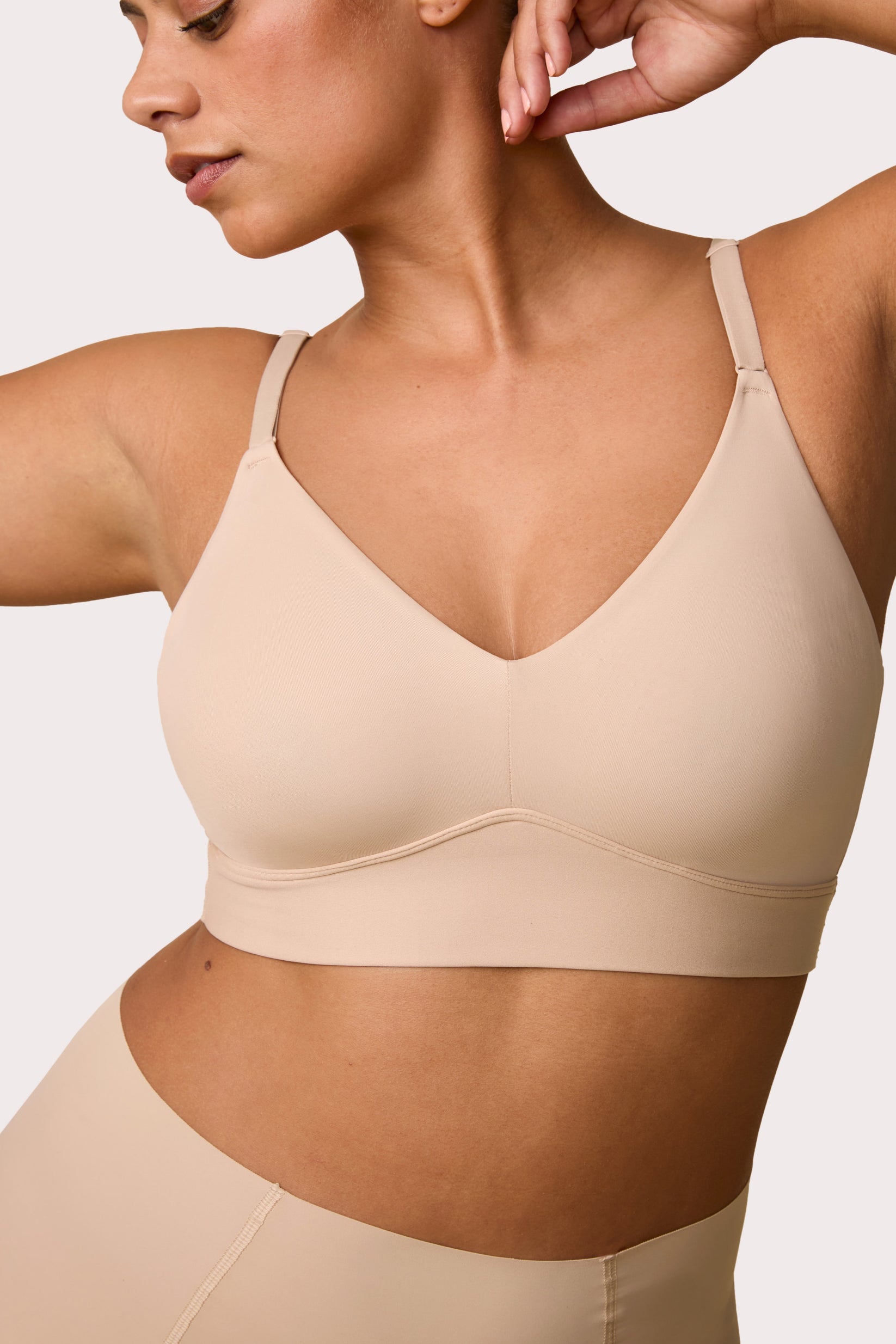 On a white studio backdrop, India wears the Bliss Triangle Bralette in Beige with the matching brief, showing the deep V neckline, smooth microfiber fabric, and wireless band.