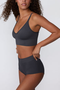 In a studio setting, Courtney wears the Ribbed Seamless Boyshort in Charcoal with a matching ribbed bralette. A side view highlights the high-rise waistband, full-coverage boyshort silhouette, and ribbed texture.