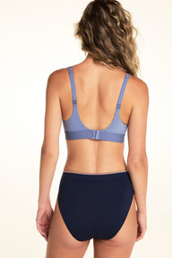 On a light studio backdrop, Alexis is shown from the back wearing the Seamless Brief in Navy with a light blue bralette. The image highlights the full back coverage, smooth seamless fabric, and contrasting waistband trim.