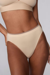 In a studio setting, Courtney wears the Smooth Seamless Brief in Beige. A close-up front view highlights the smooth fabric, high-leg silhouette, and contrast trim waistband.