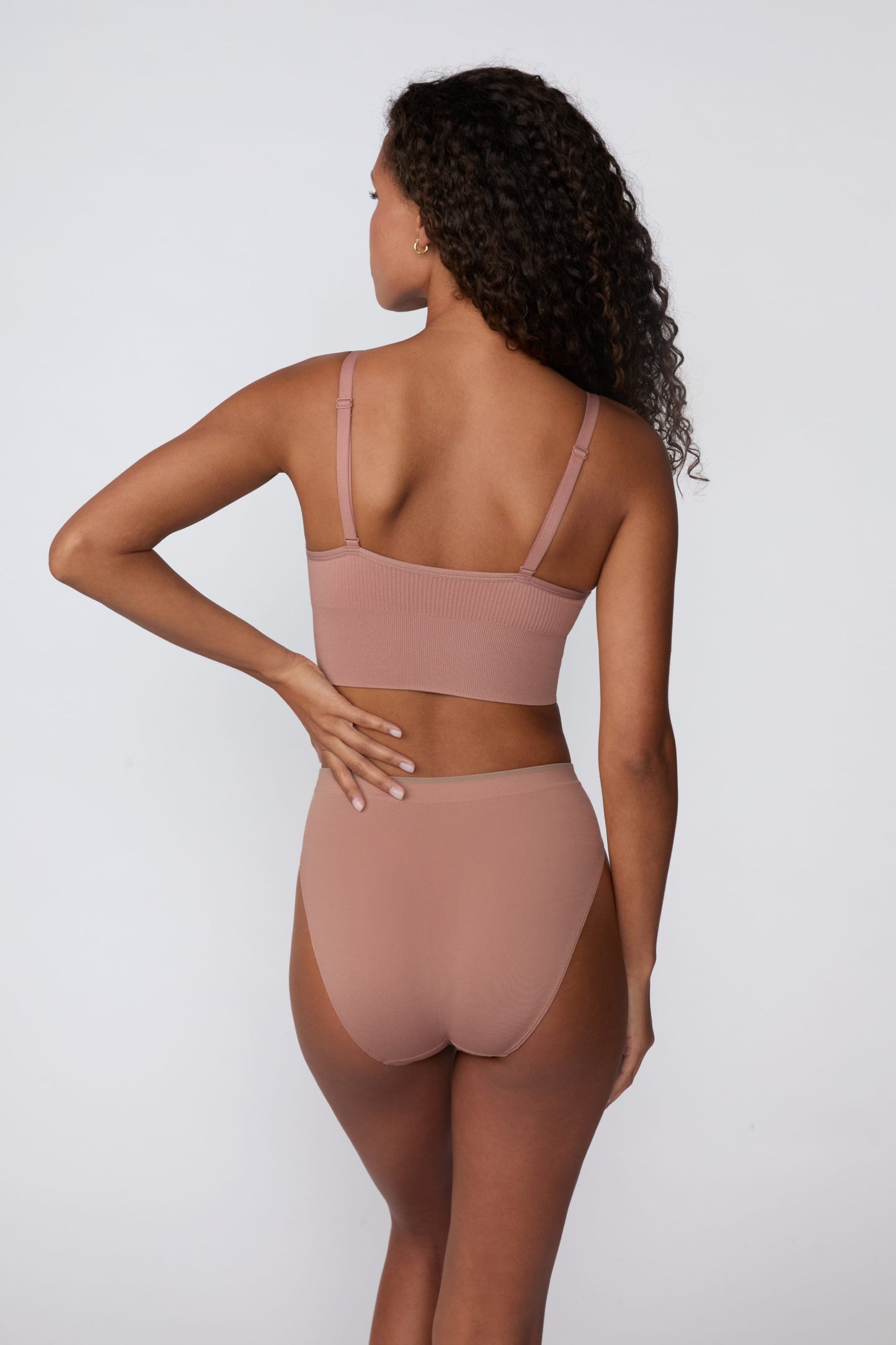 In a studio setting, Courtney wears the Smooth Seamless Brief in Plum with the matching Seamless Scoop Bralette in Plum. The back view highlights the full back coverage, smooth finish, and contrast trim waistband.