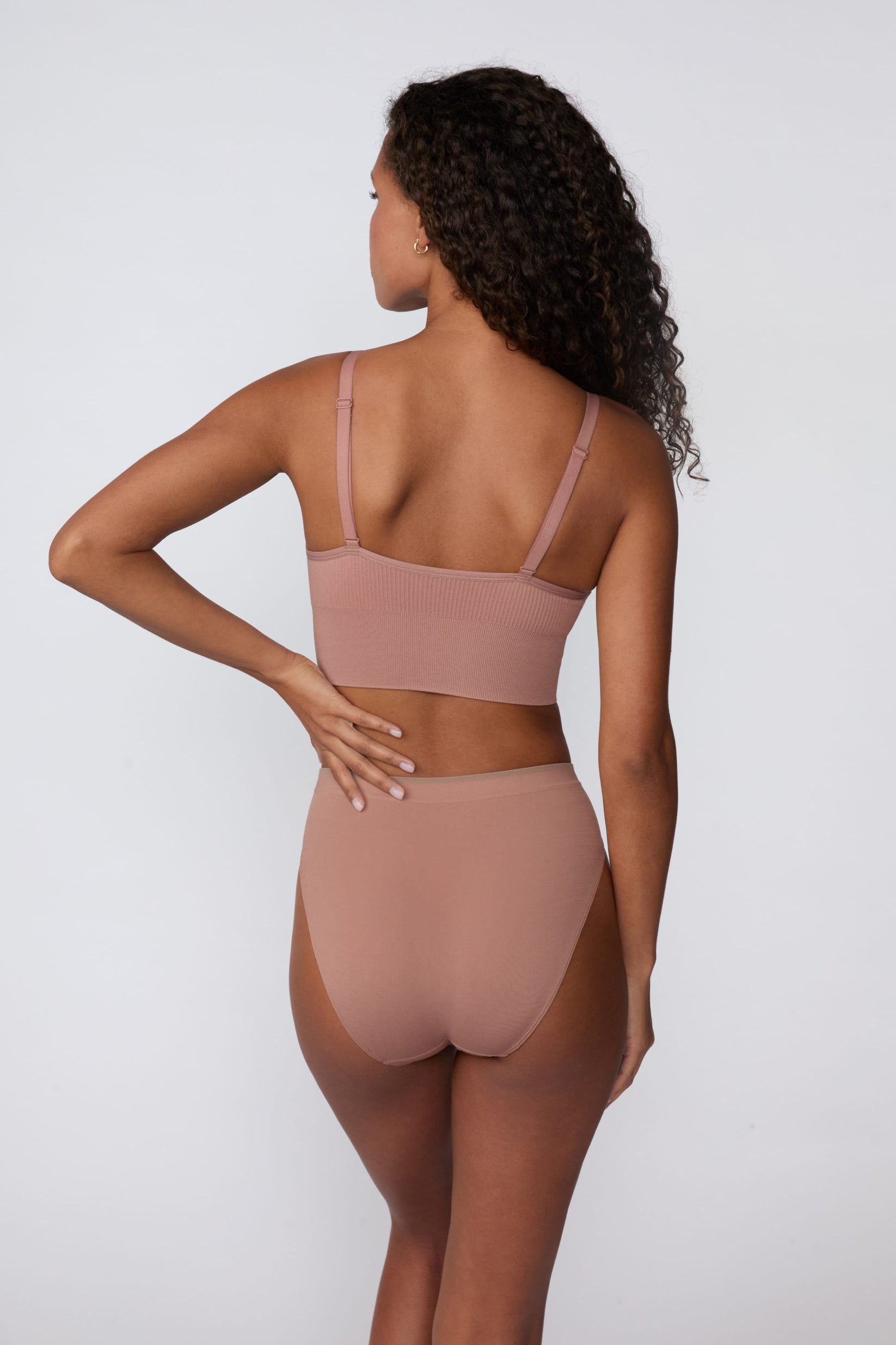 In a studio setting, Courtney wears the Smooth Seamless Brief in Plum with the matching Seamless Scoop Bralette in Plum. The back view highlights the full back coverage, smooth finish, and contrast trim waistband.