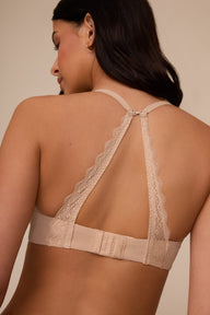 On a neutral studio backdrop, Marcela wears the Base Lace T-Shirt Bra in Beige. The back view showcases the convertible racerback feature, adjustable straps, hook-and-eye closure, and lace detailing along the back straps.