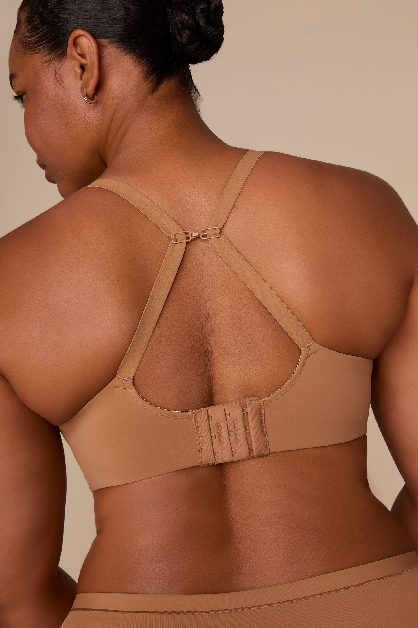 On a neutral beige backdrop, Zarria wears the Base Wirefree T-Shirt Bra in Tan with matching underwear, highlighting the smooth cups, wireless design, and adjustable straps.