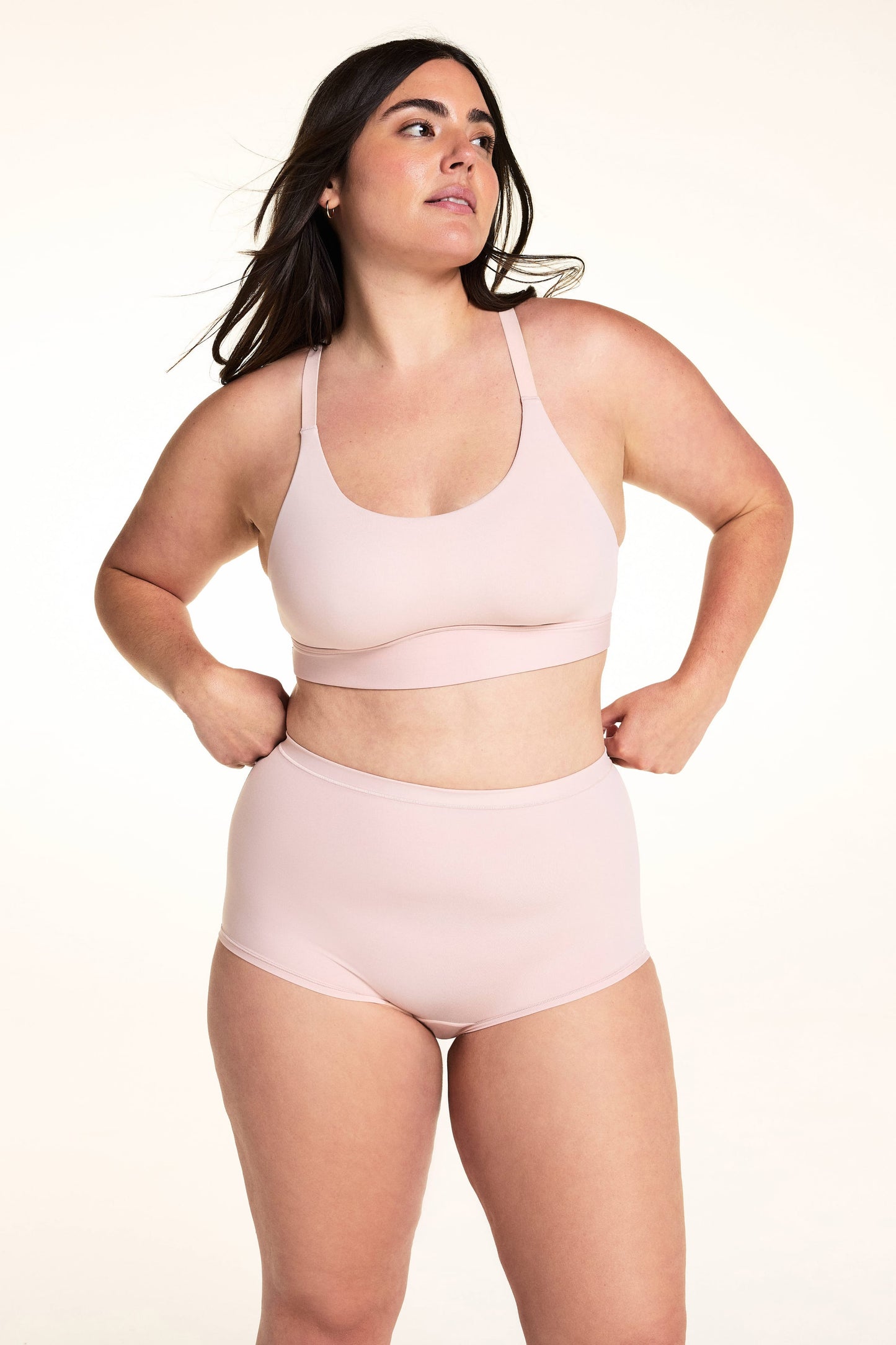 On a light studio backdrop, Alessandra wears the Bliss Racerback Bralette in Ember Rose with matching high-rise bottoms. The full-body image highlights the scoop neckline, smooth fabric, adjustable straps, and wide comfort band.