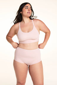 On a light studio backdrop, Alessandra wears the Bliss Racerback Bralette in Ember Rose with matching high-rise bottoms. The full-body image highlights the scoop neckline, smooth fabric, adjustable straps, and wide comfort band.
