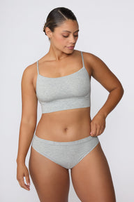 In a studio setting, India wears the Cloud Cotton Thin Strap Bralette in Heather Grey with matching underwear. The front view highlights the straight neckline, thin adjustable straps, and soft cotton fabric.