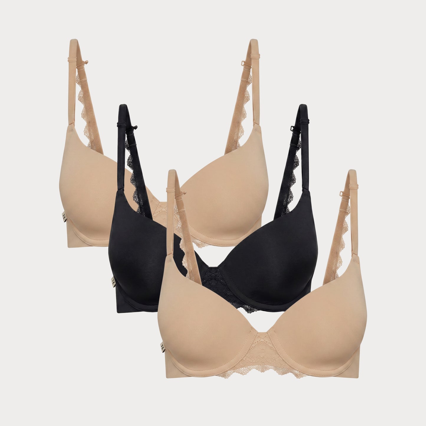 Flat lay image of 3 Base Lace T-Shirt Bras in Beige and Black showcasing the soft lace detail at the center and along the back strap.